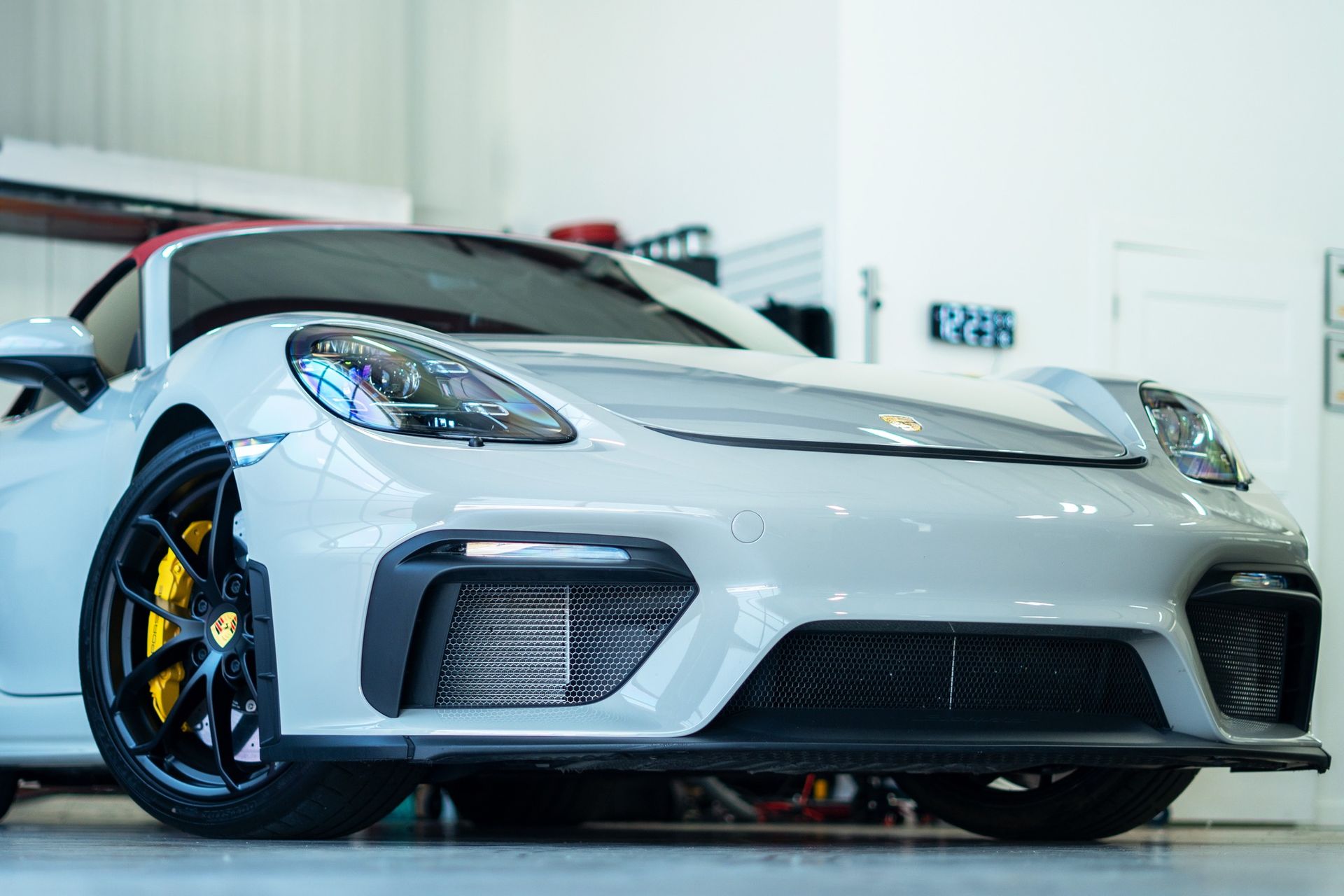 A white Porsche Boxster convertible with yellow brake calipers parked inside a garage.