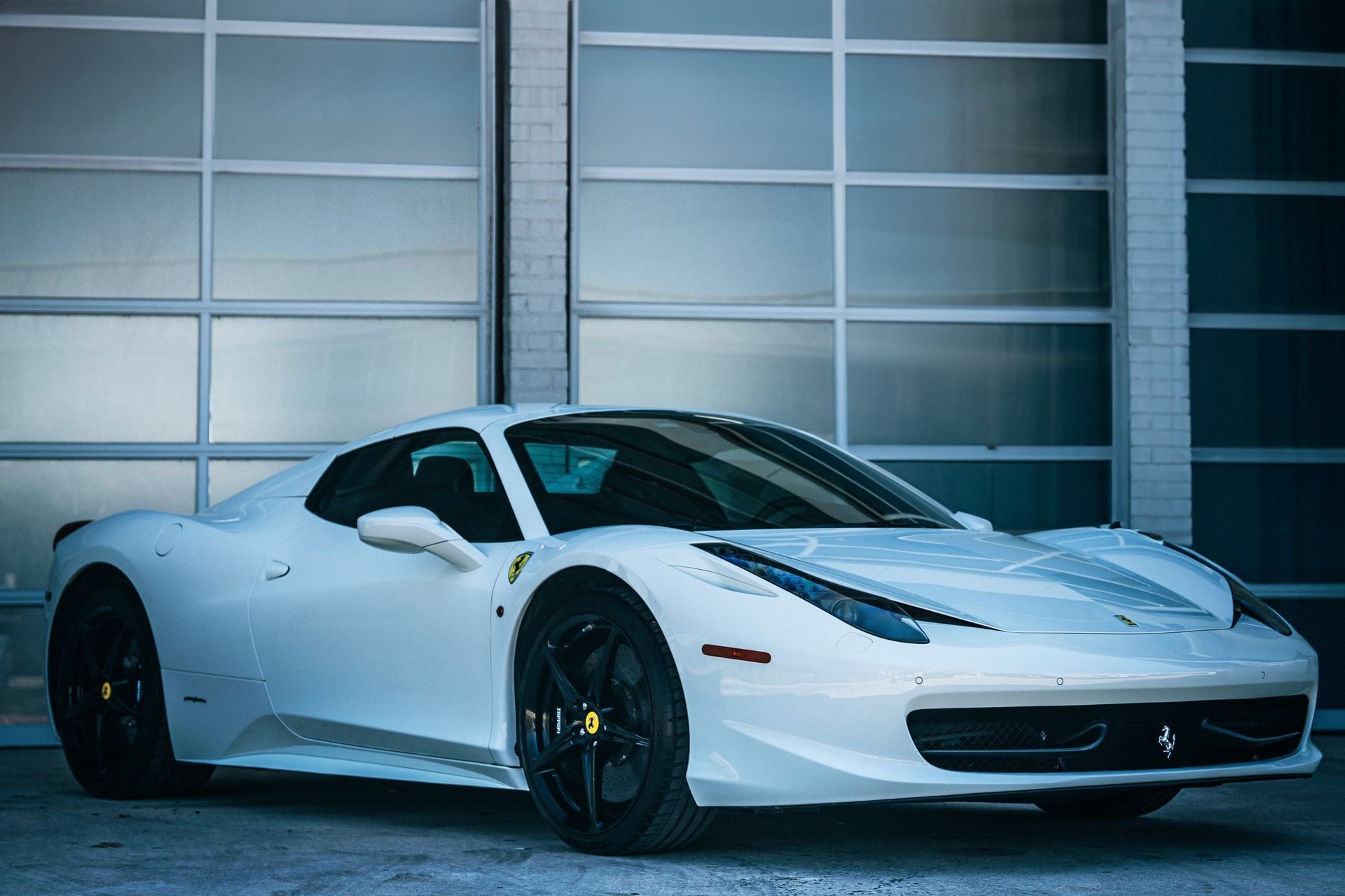 White Ferrari sports car parked in front of a garage with black wheels.