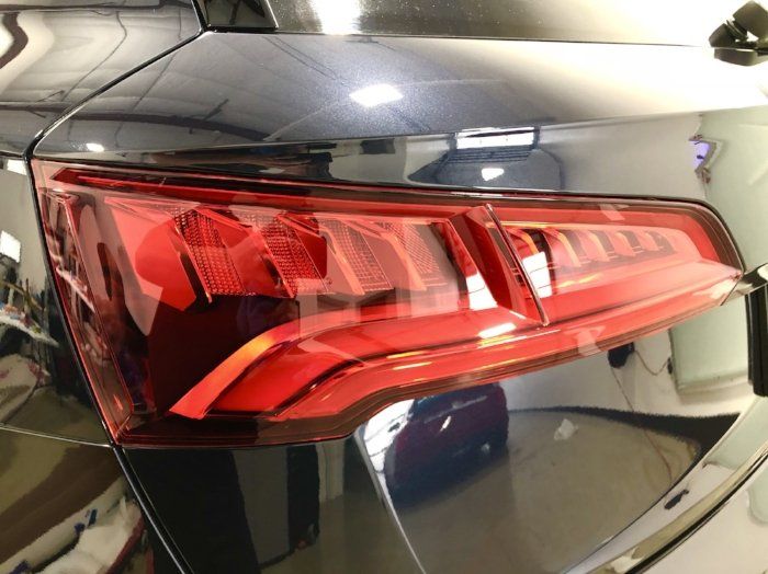 A black car with a red tail light is parked in a garage.
