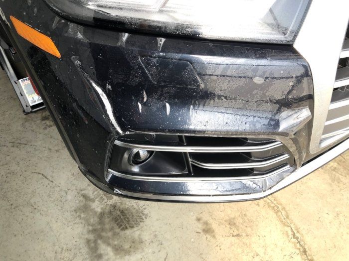 A black car with a broken bumper is parked in a garage.