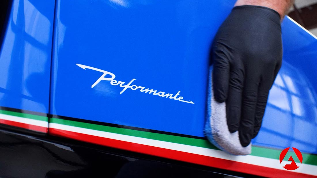 A gloved hand applies detailing product to blue sports car's