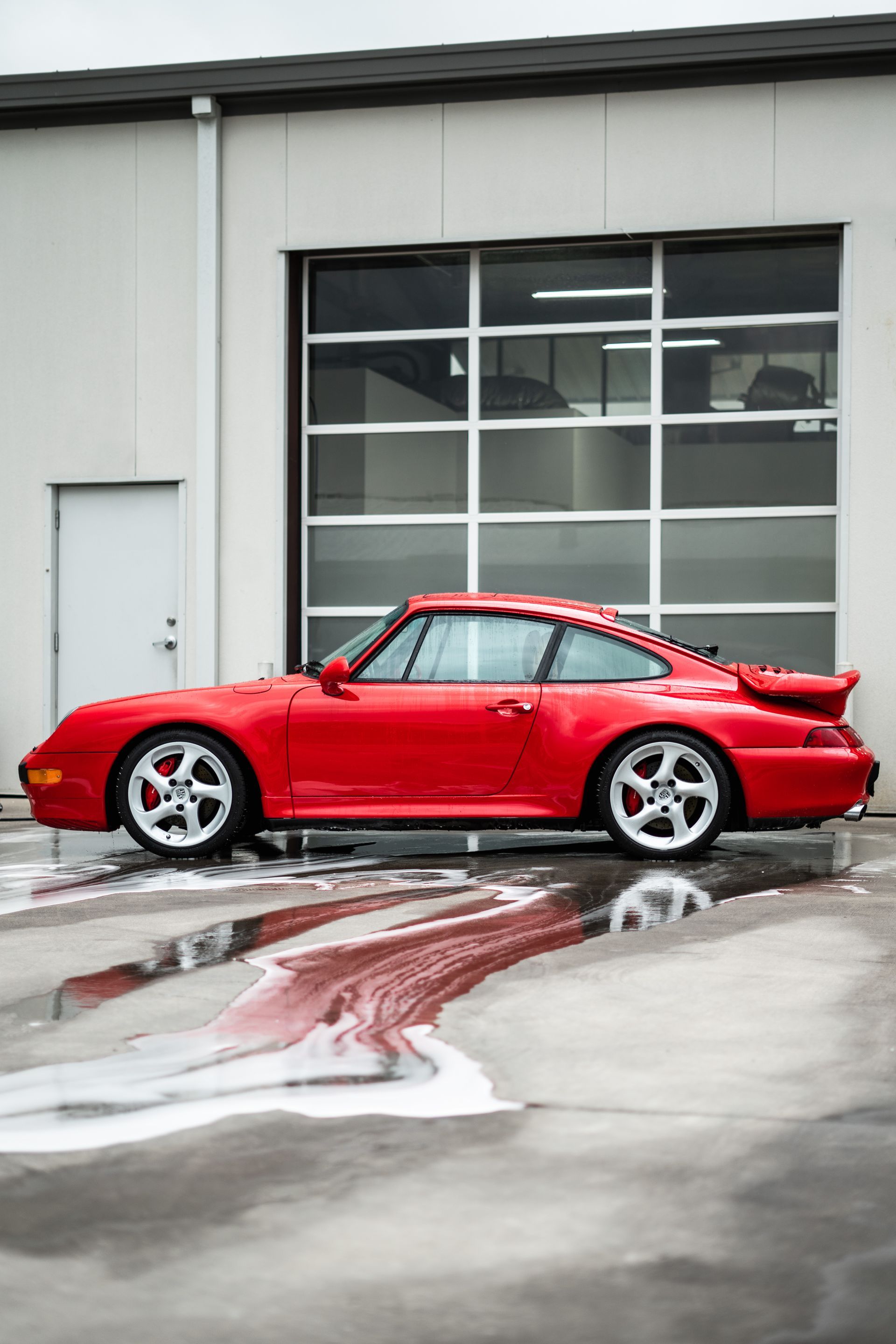 Red Porsche 911 parked outside a garage, surrounded by soapy water.
