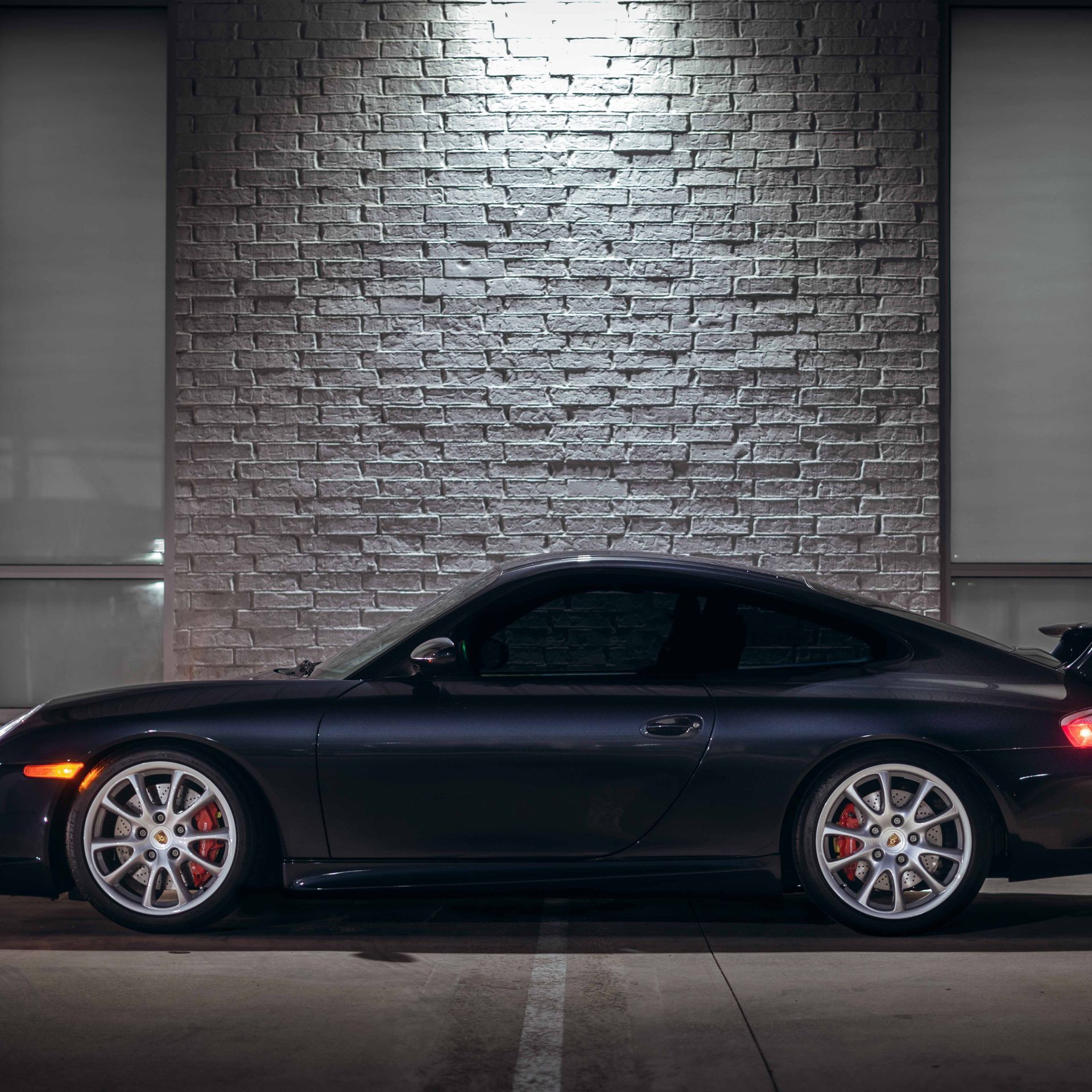 Dark gray Porsche sports car parked in front of a brick wall at night.
