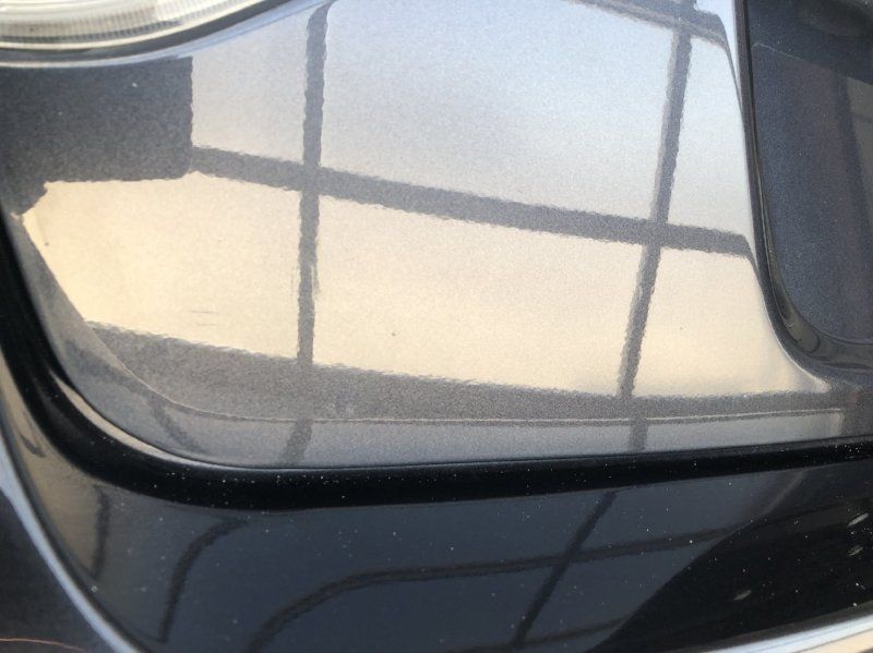 A close up of a car 's bumper with a reflection of a window