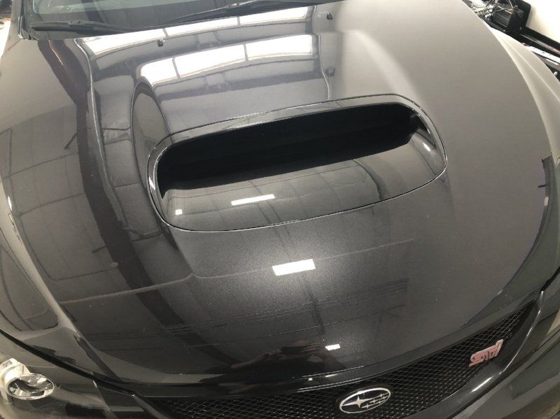 A black car with a hood scoop is parked in a garage.