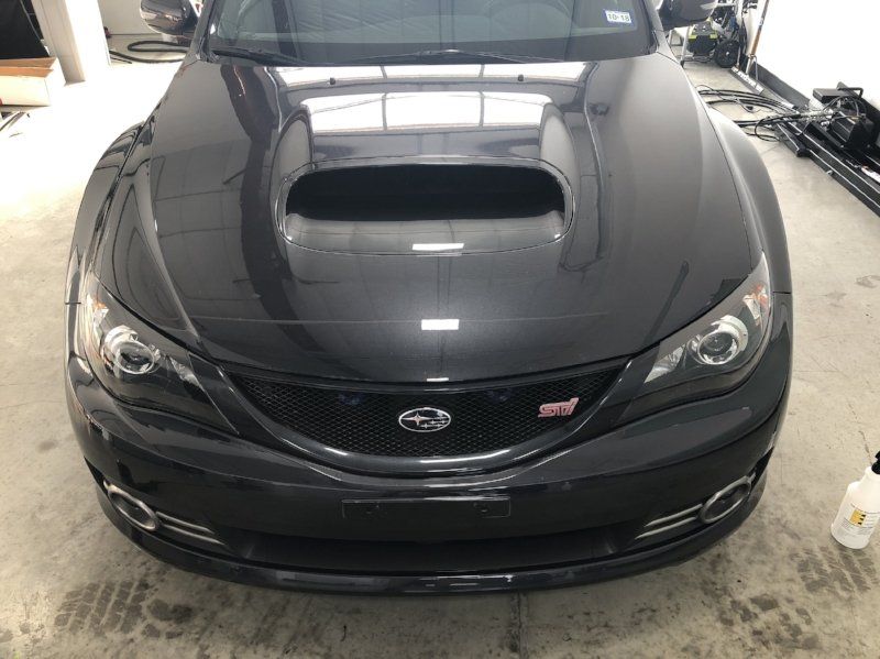 A black subaru is parked in a garage with the hood up