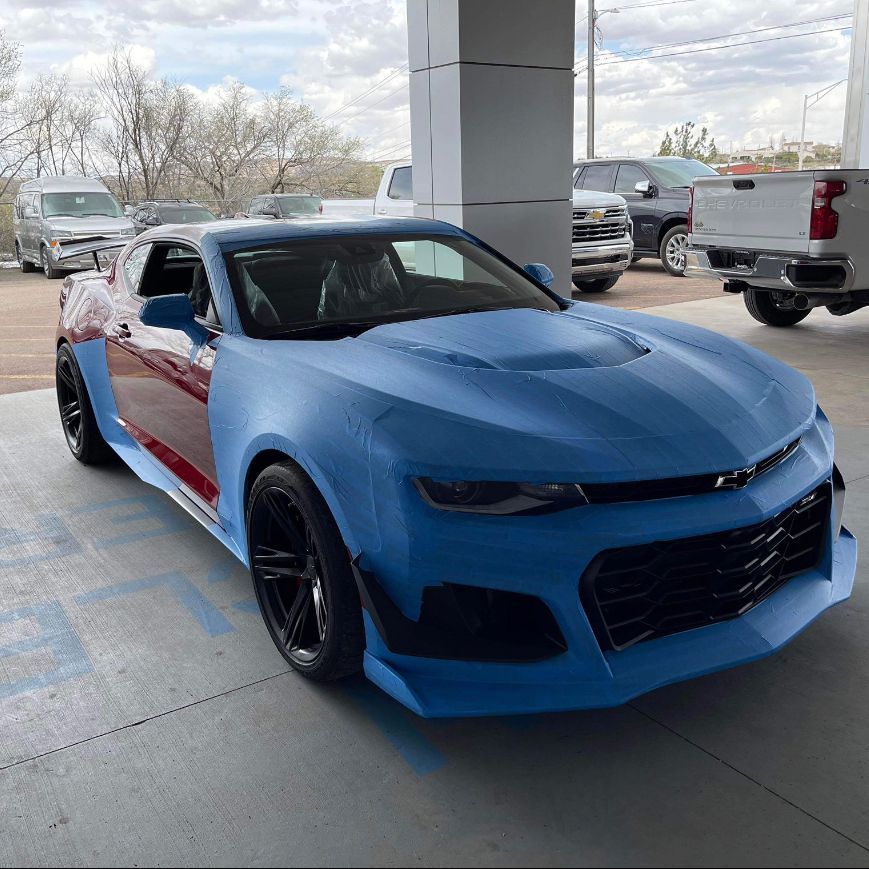 A blue car is parked in a parking lot next to a truck.