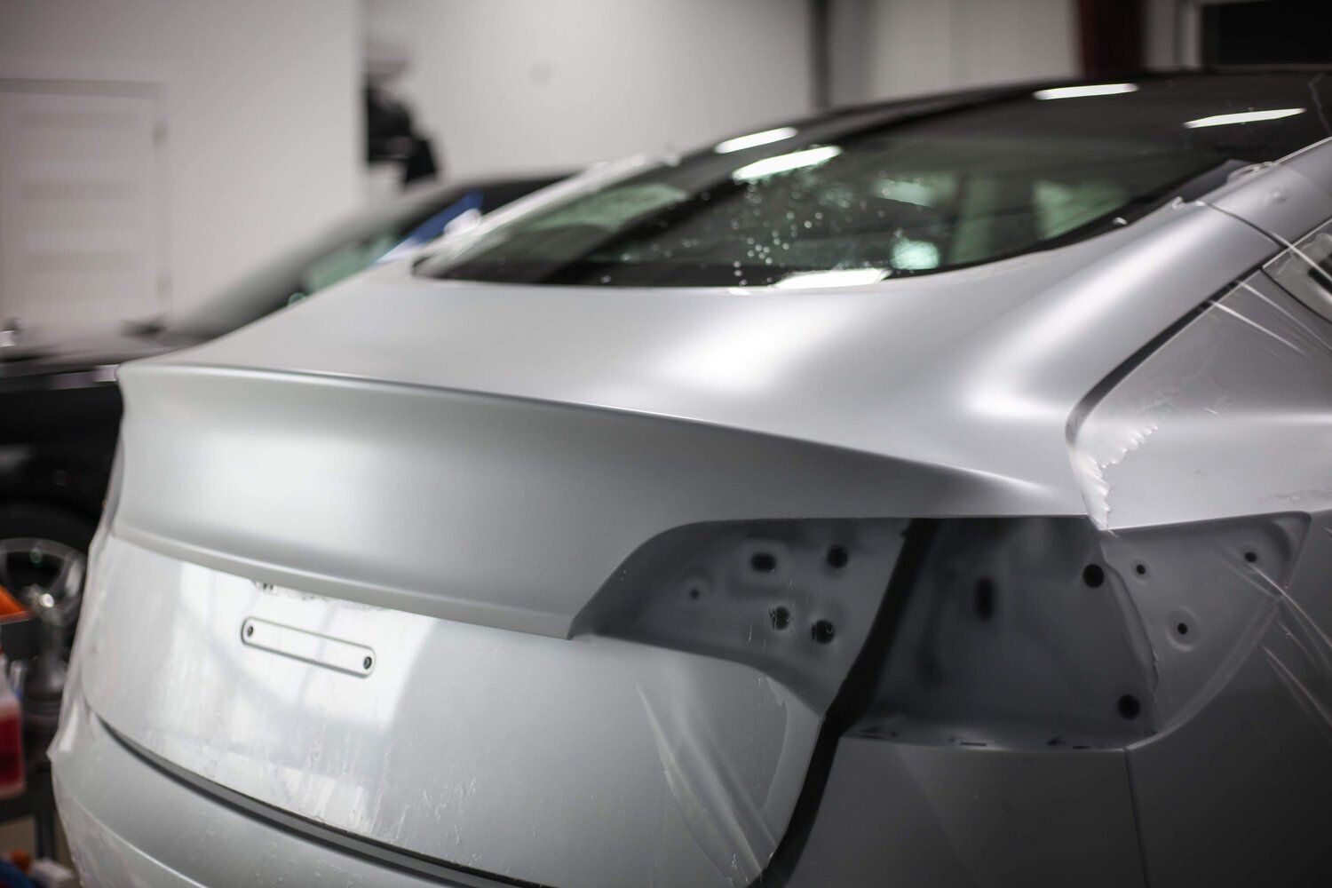A white car is wrapped in a white wrap in a garage.