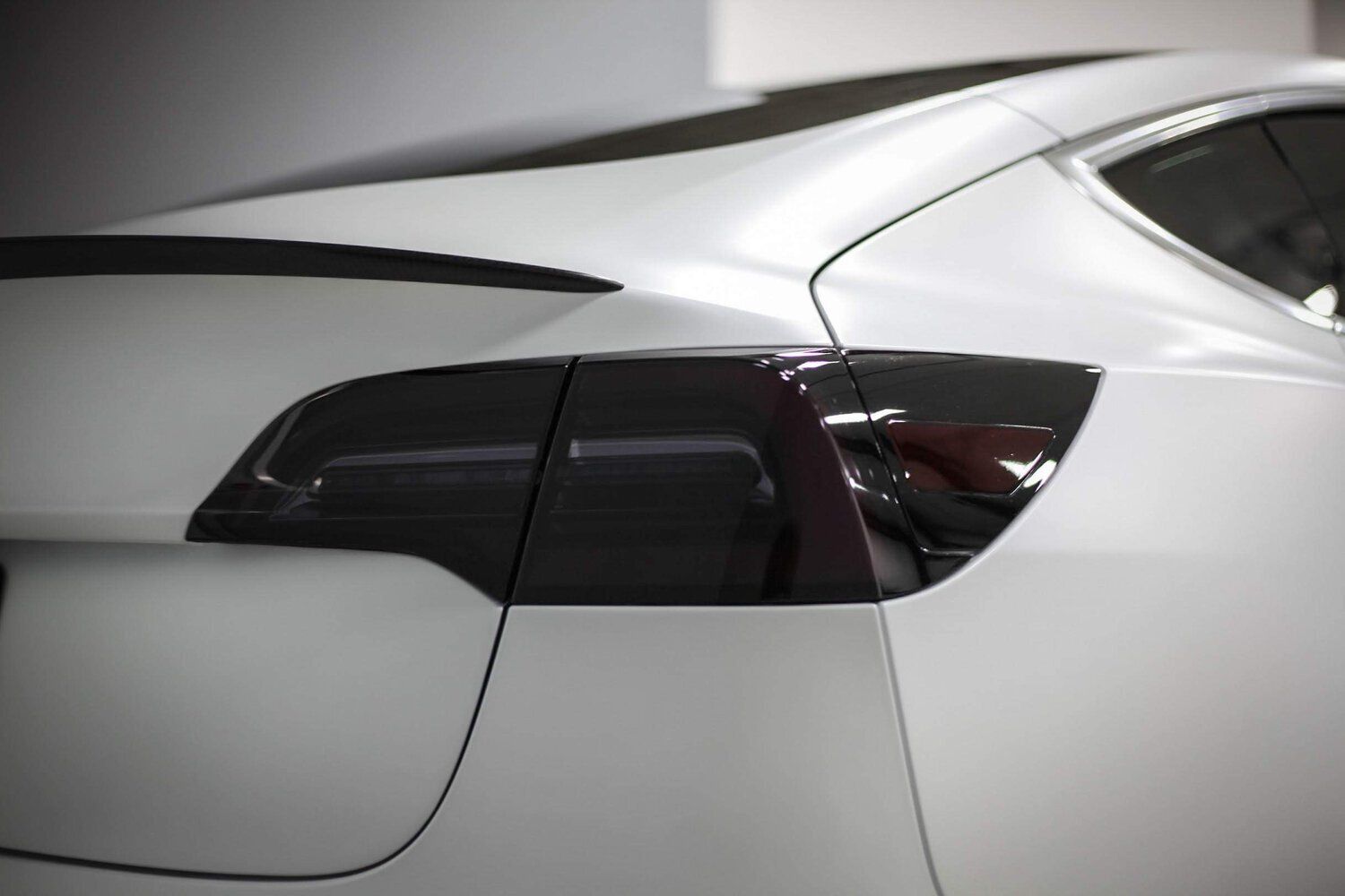 A white tesla model 3 with black tail lights is parked in a garage.