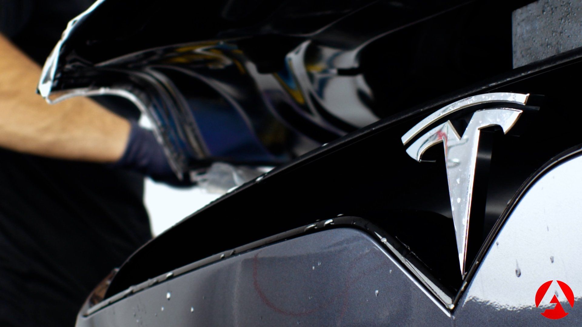 Black Tesla car being detailed; a person is applying a film to the hood.