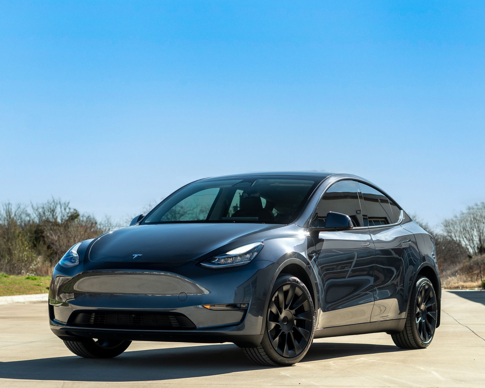 A gray Tesla Model Y SUV parked on a road under a clear blue sky.