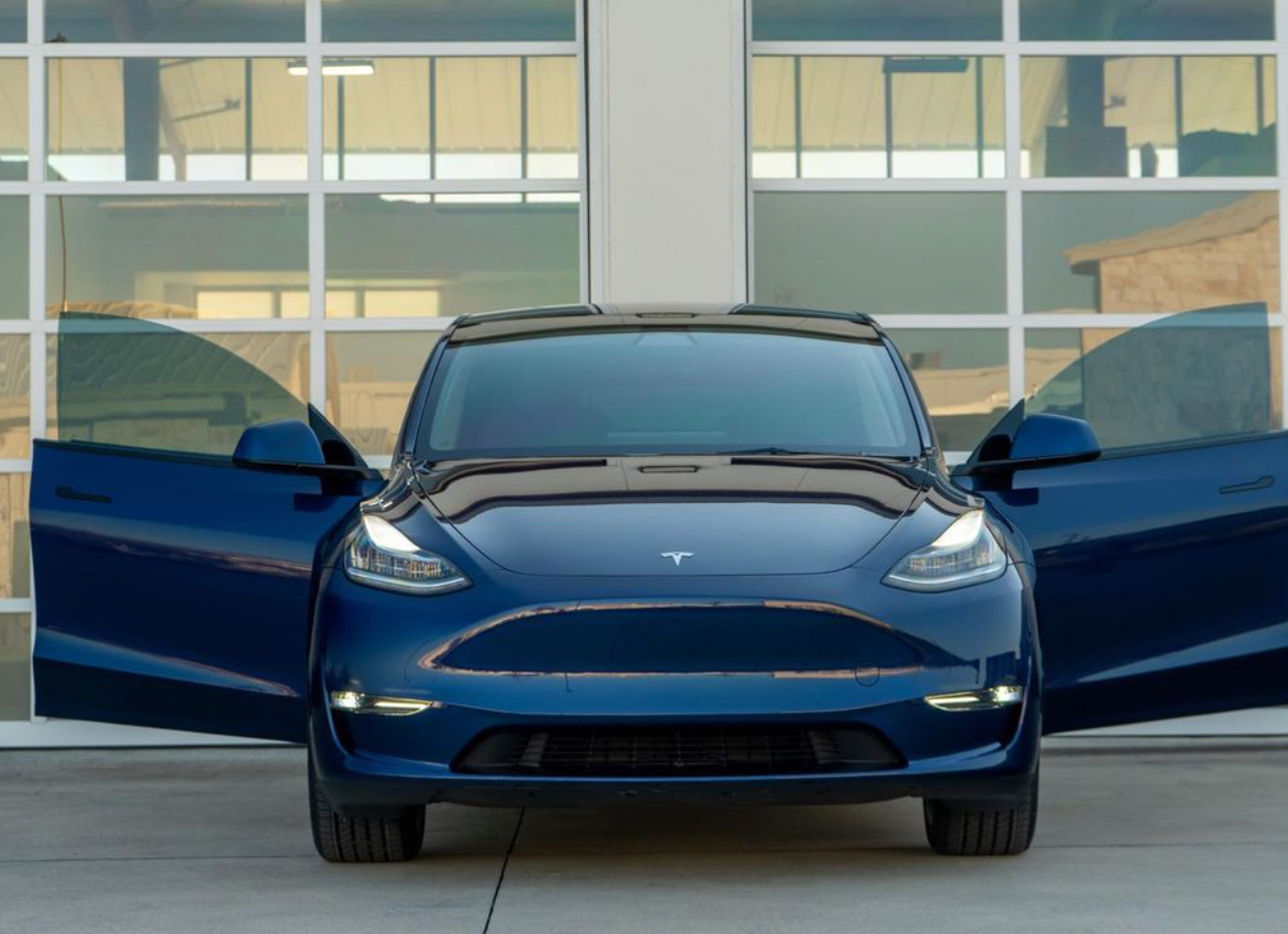 A blue tesla model y is parked in a parking lot with its doors open.