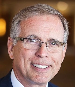 A man wearing glasses and a suit is smiling for the camera.