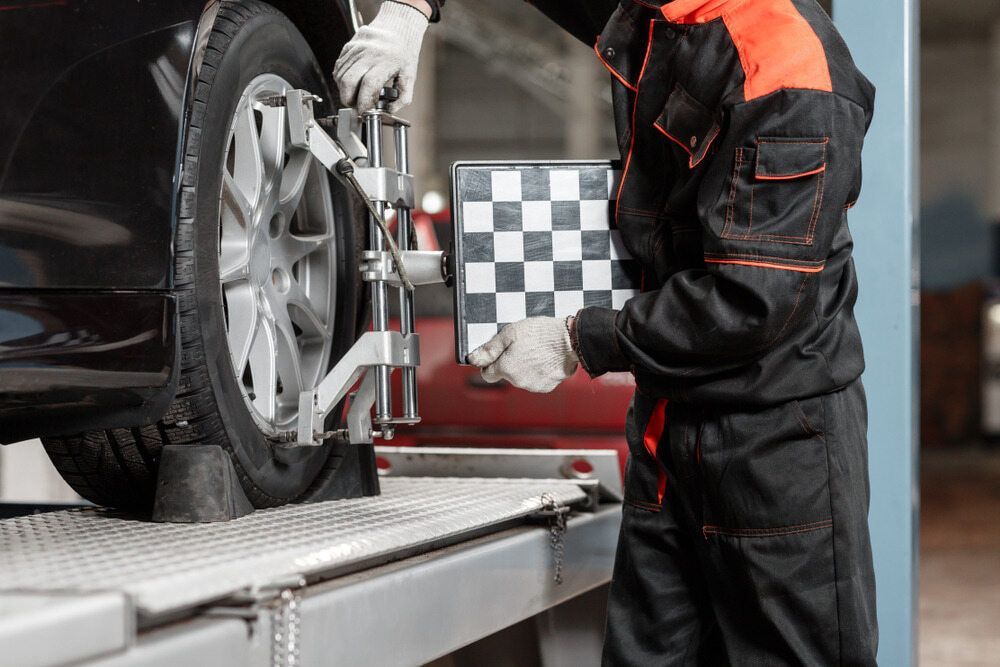 A Man Is Adjusting A Car Tire In A Garage While Holding A Checkered Board — Macgregor Auto In Belconnen, ACT