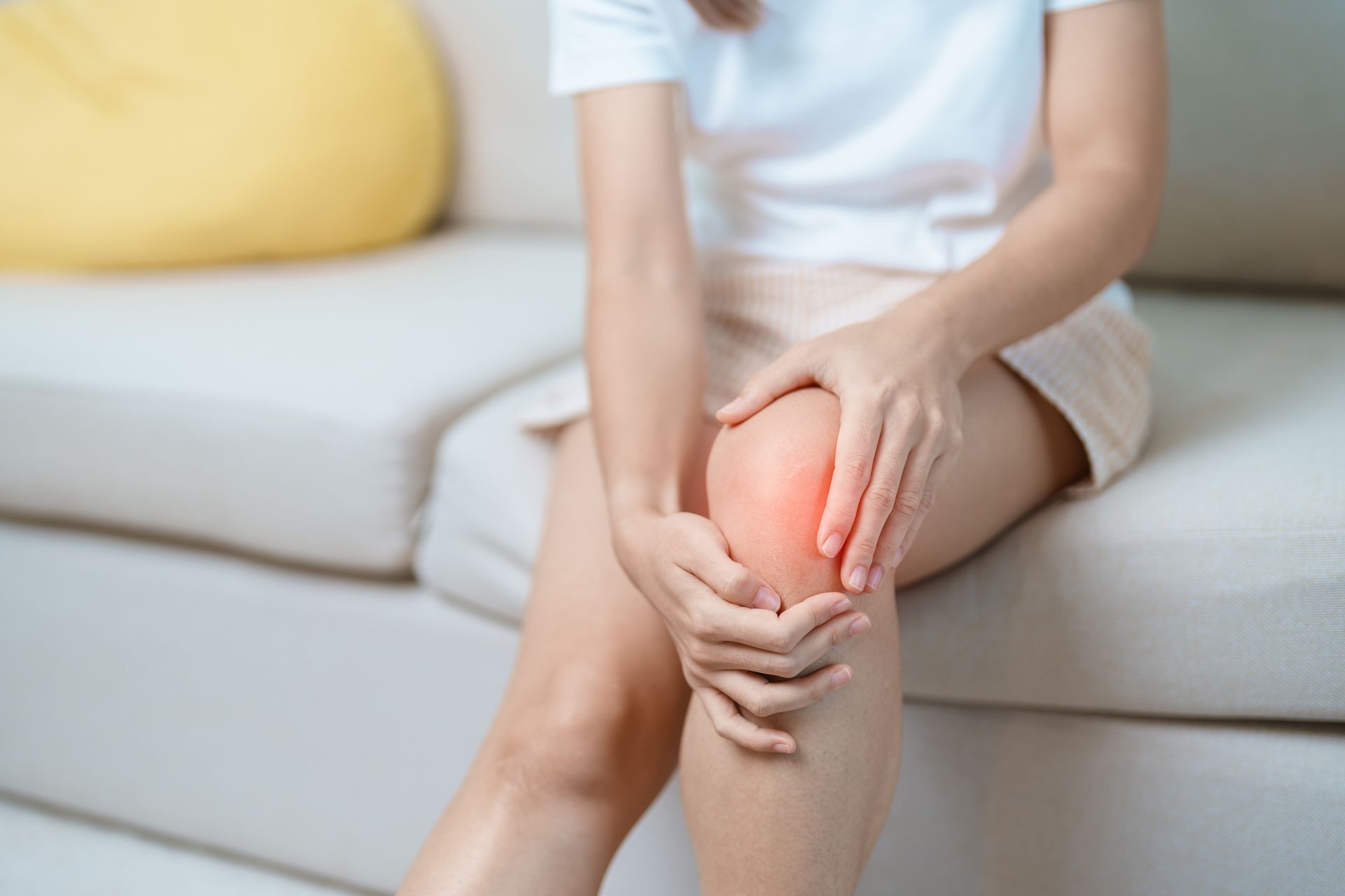 Person sitting on a couch holding a glowing knee in pain
