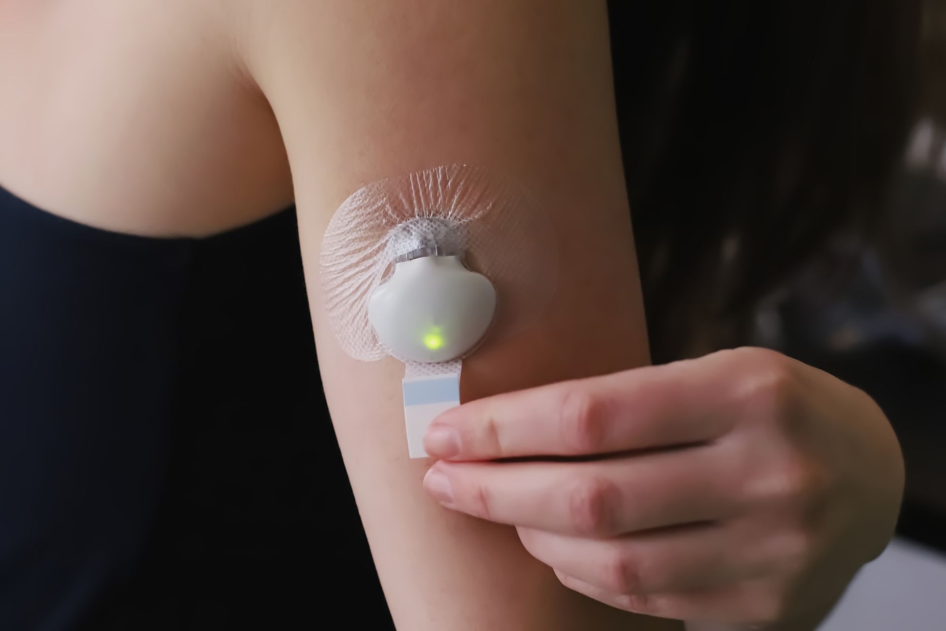 Arm with a wearable sensor patch and a hand adjusting the adhesive sensor.
