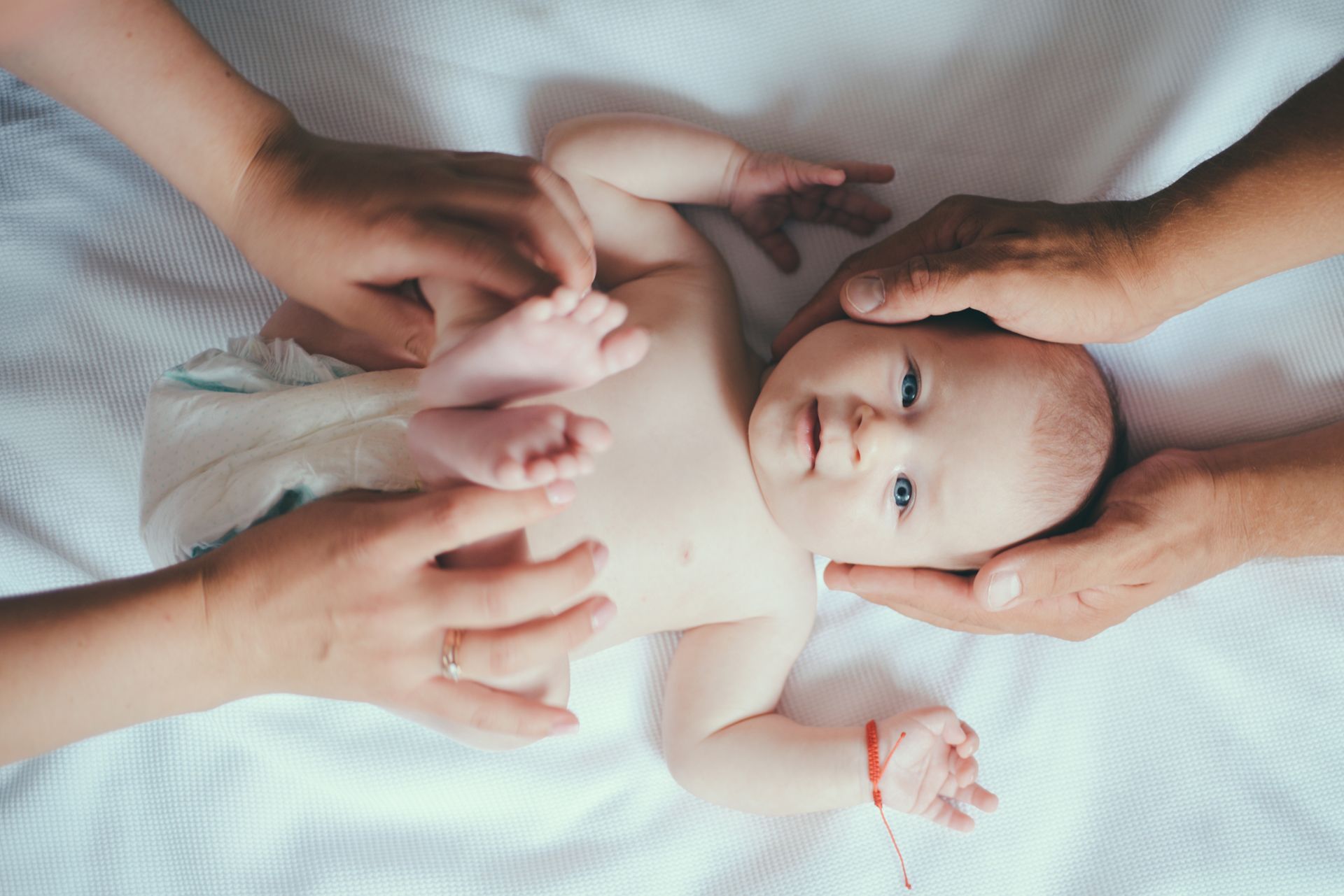 Newborn baby lying on a white blanket, gently touched by several adult hands