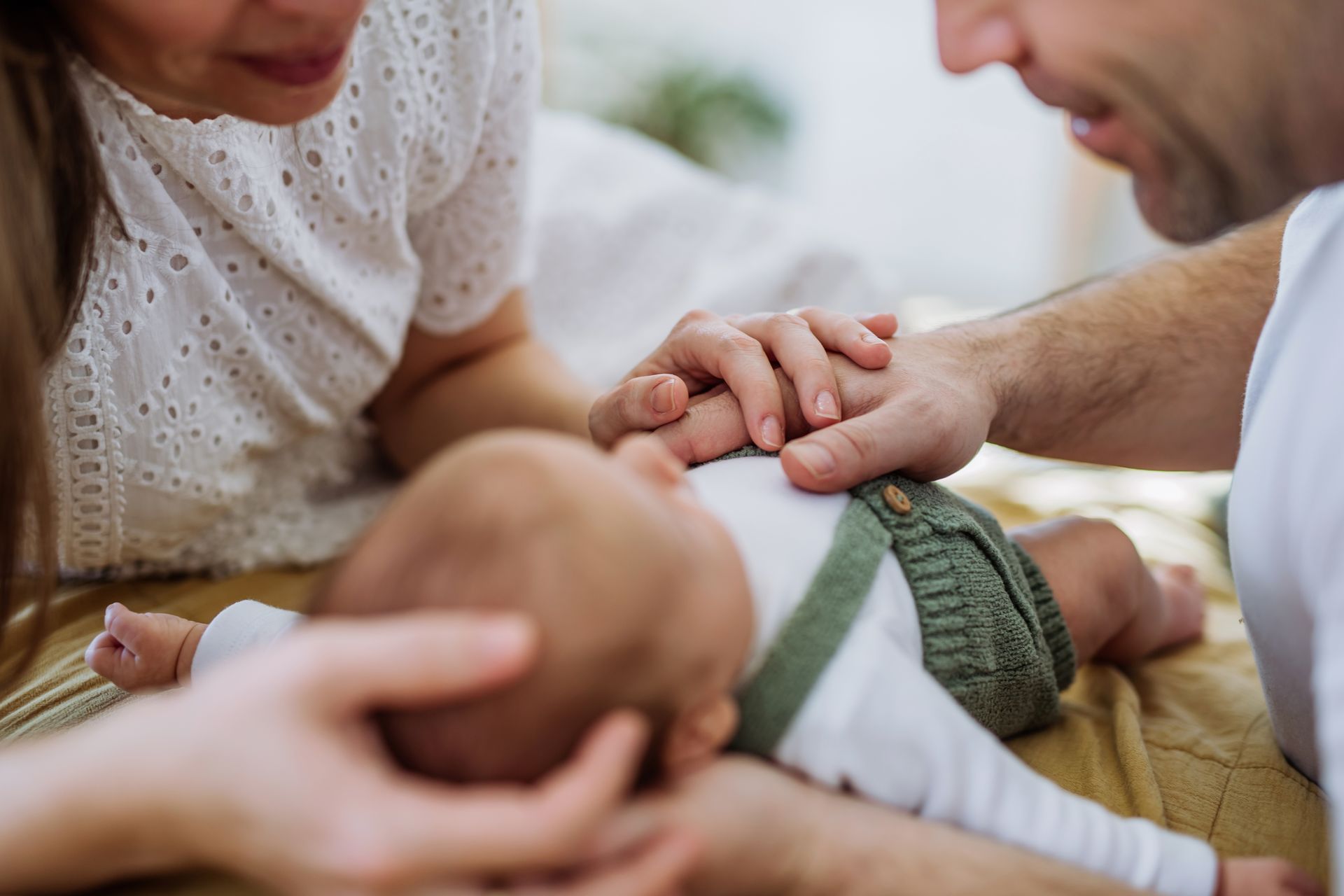 Parents holding a baby’s hands as they lean over and smile in a cozy home setting
