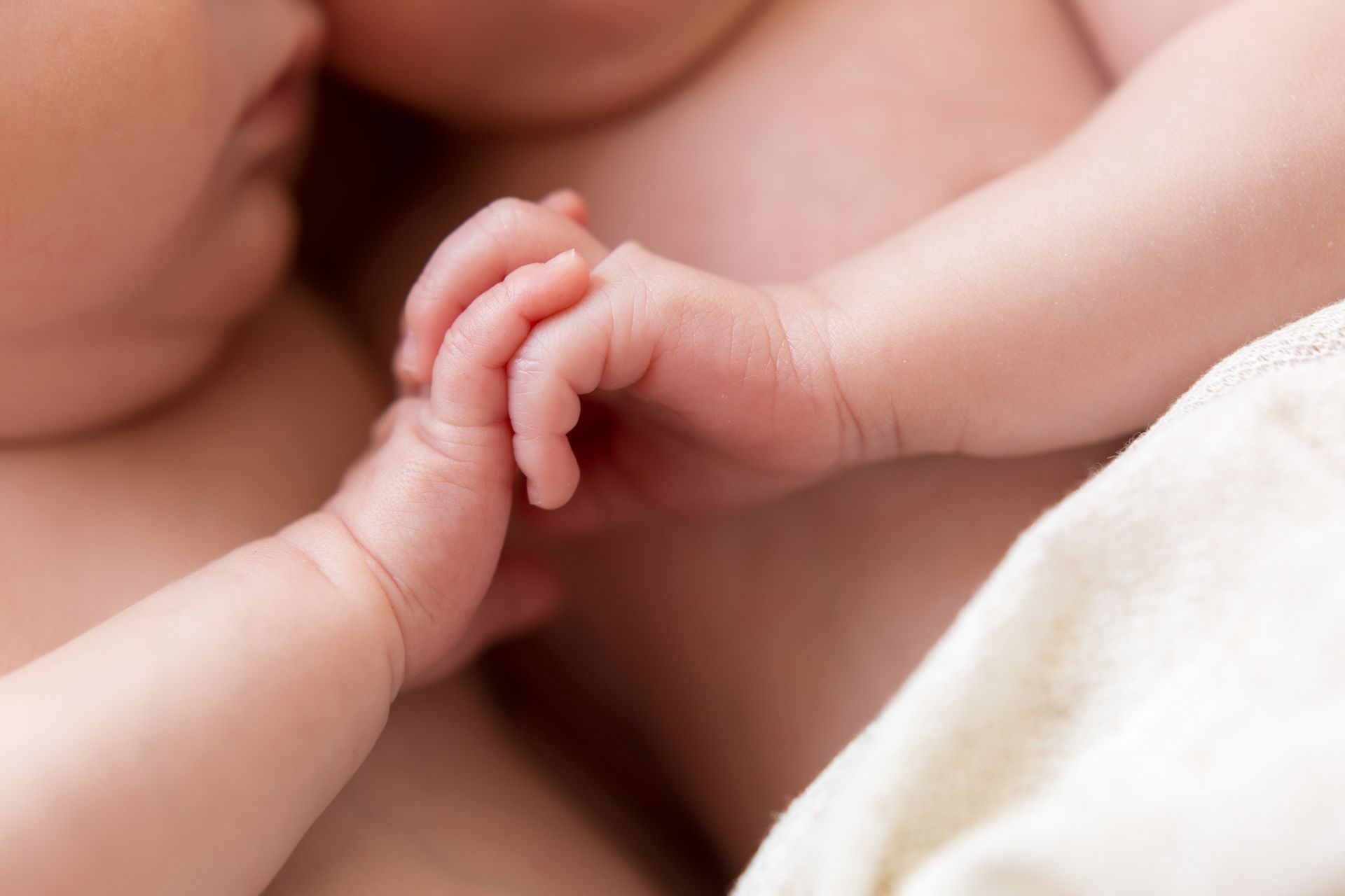 Two babies holding hands, close-up with soft beige blankets