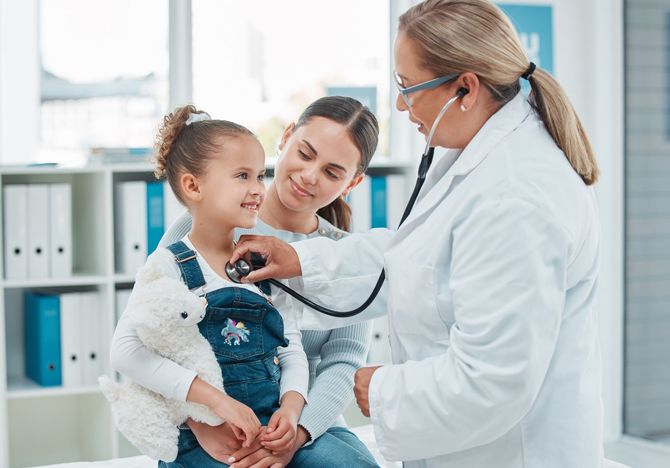 Doctor examining a young child with a stethoscope in a bright clinic, with a parent nearby