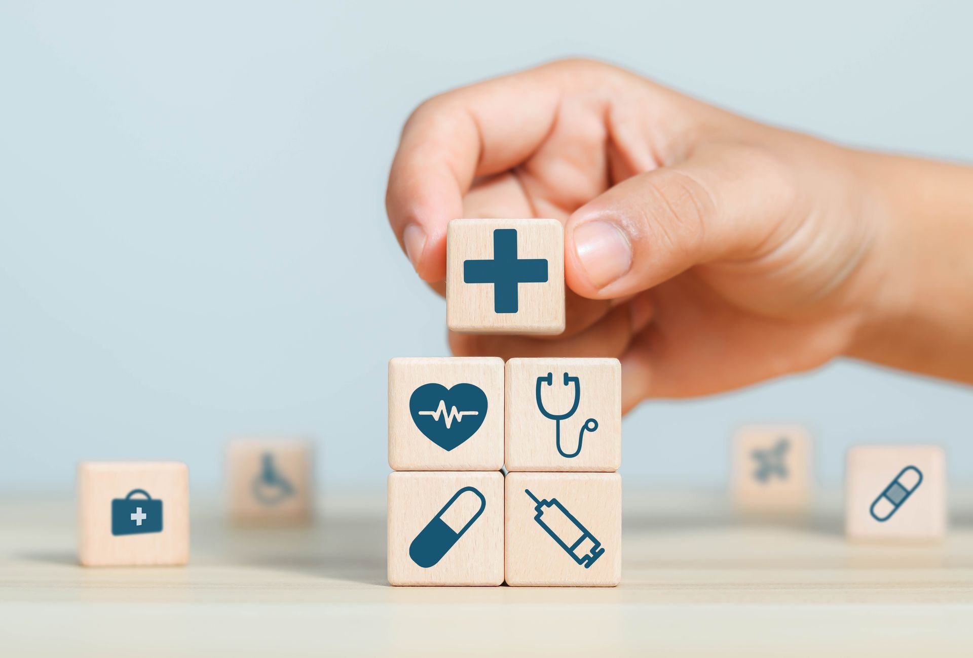 Hand placing a medical cross block atop healthcare icon blocks on a table