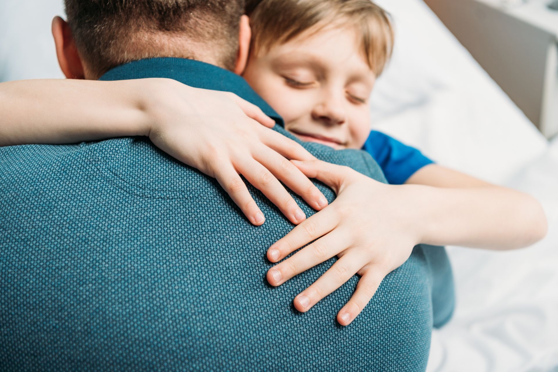 Child hugging an adult from behind on a couch, both in blue shirts, with a calm, affectionate expression