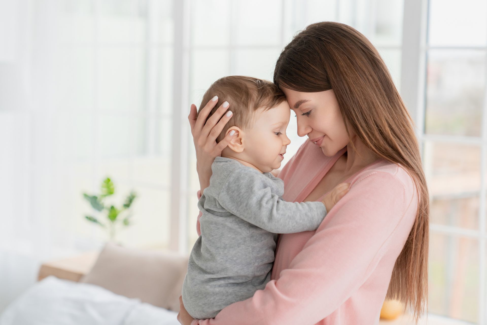 Woman holding a small child indoors, touching foreheads in a tender embrace.