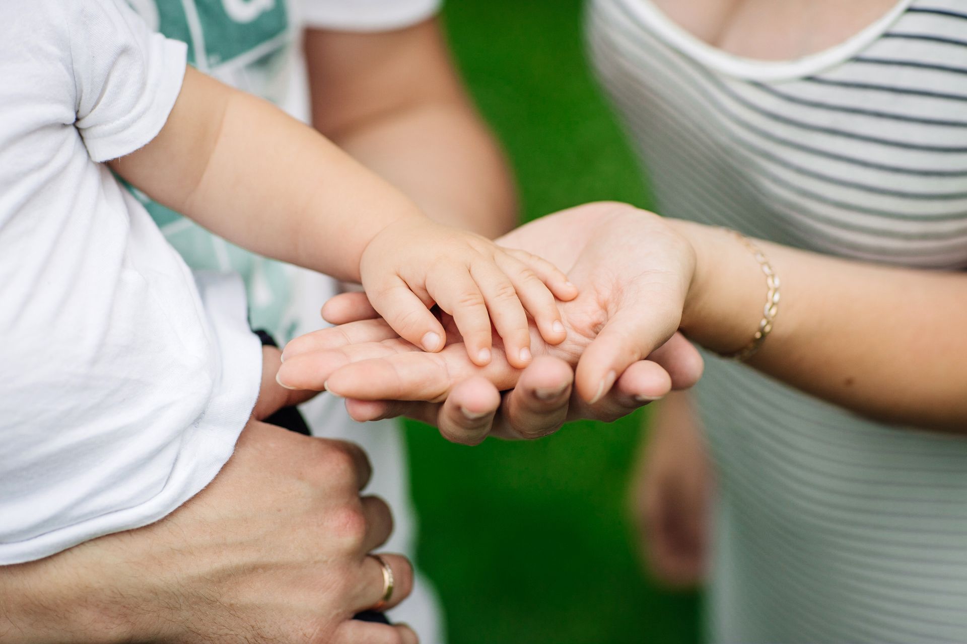 Hands stacked together in a supportive group gesture outdoors, with a child’s hand on top.