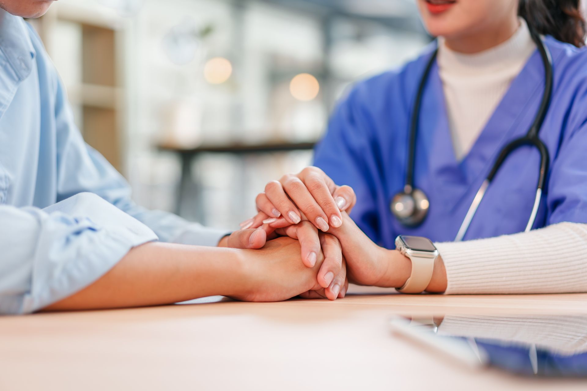 Healthcare worker holding a patient’s hand at a hospital desk, offering comfort and support