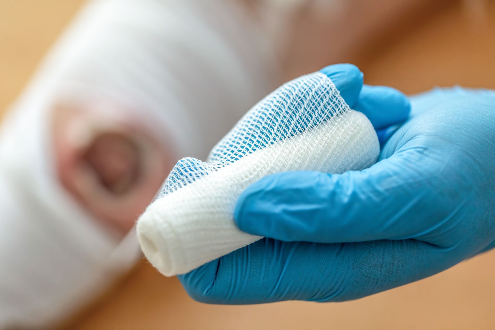 Blue-gloved hand holding a white bandage over a wrapped forearm