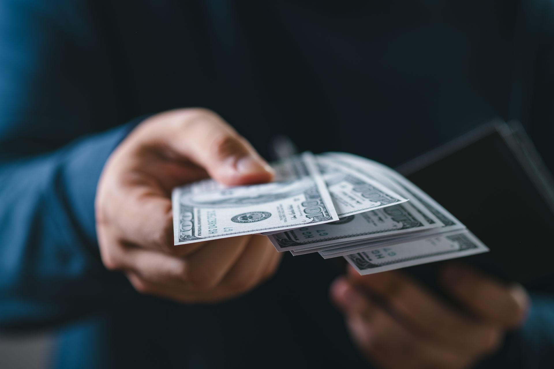 Hand holding U.S. dollar bills and a wallet against a dark background