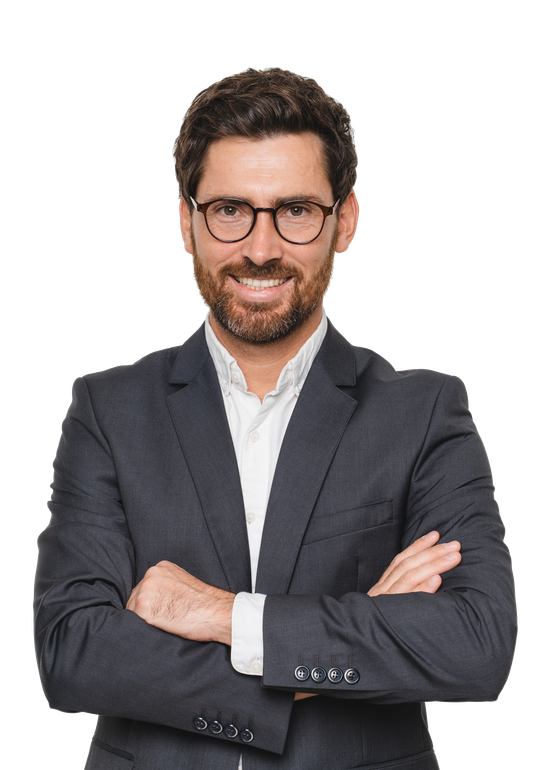 Man in a dark suit with glasses, arms crossed, smiling against a plain white background