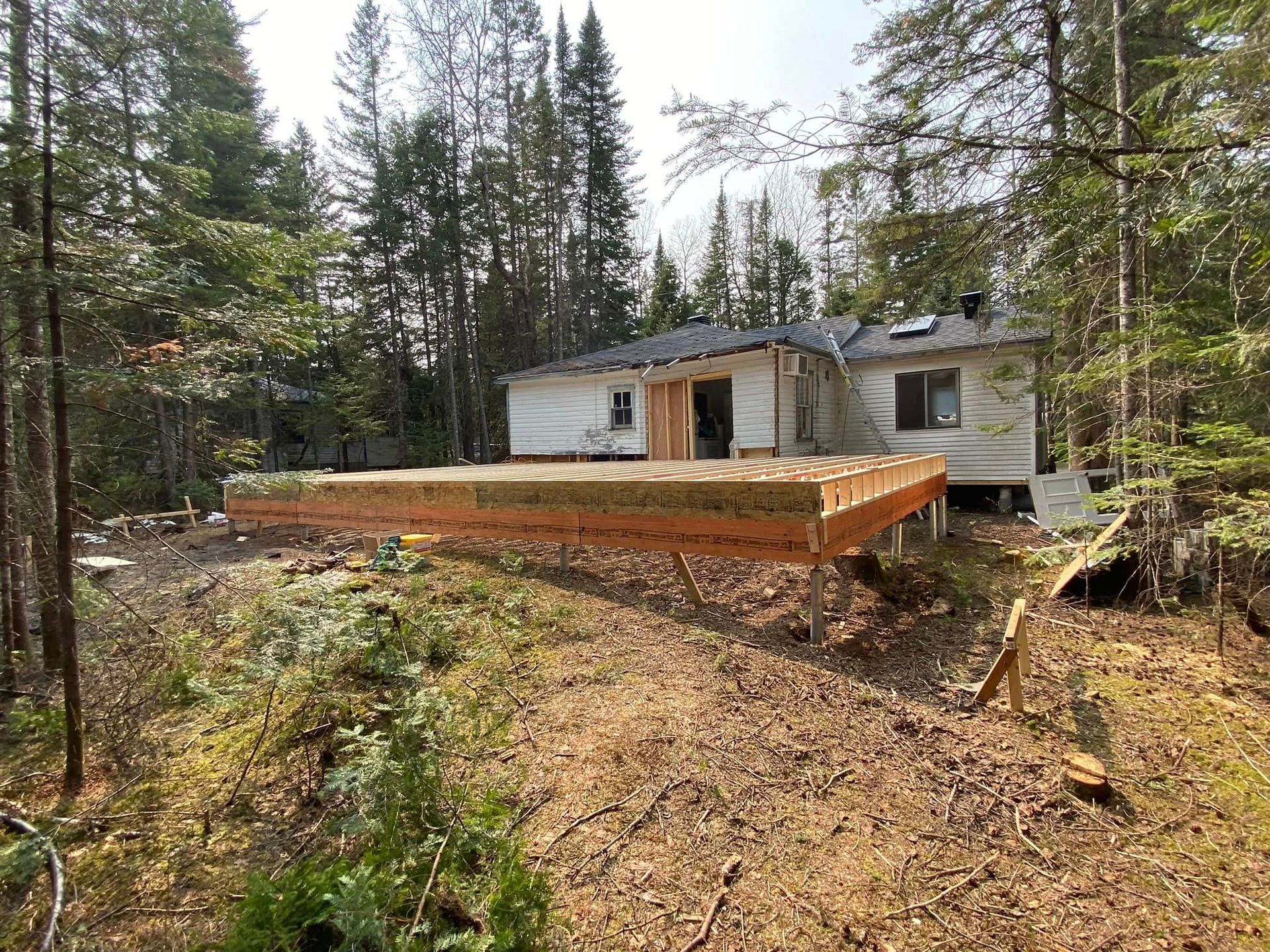 A wooden deck is being built in front of a house in the woods.