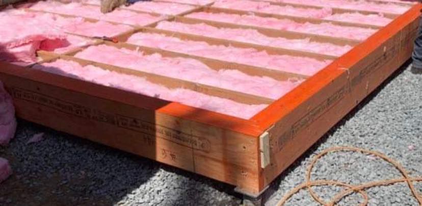 A wooden box filled with pink insulation is sitting on the ground.