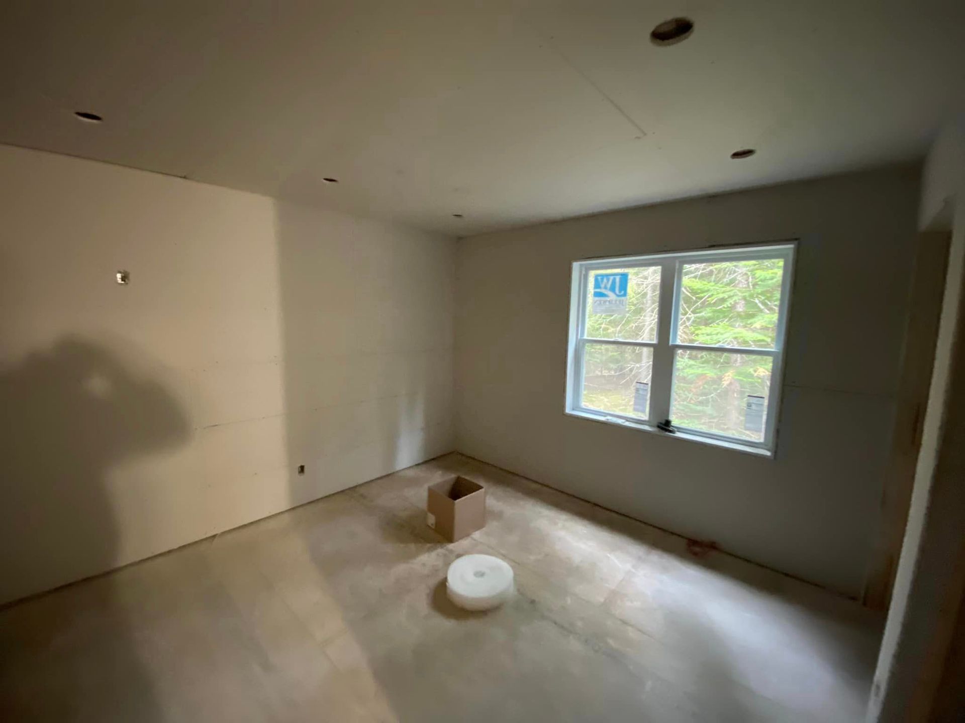 An empty room with two windows and a box on the floor.