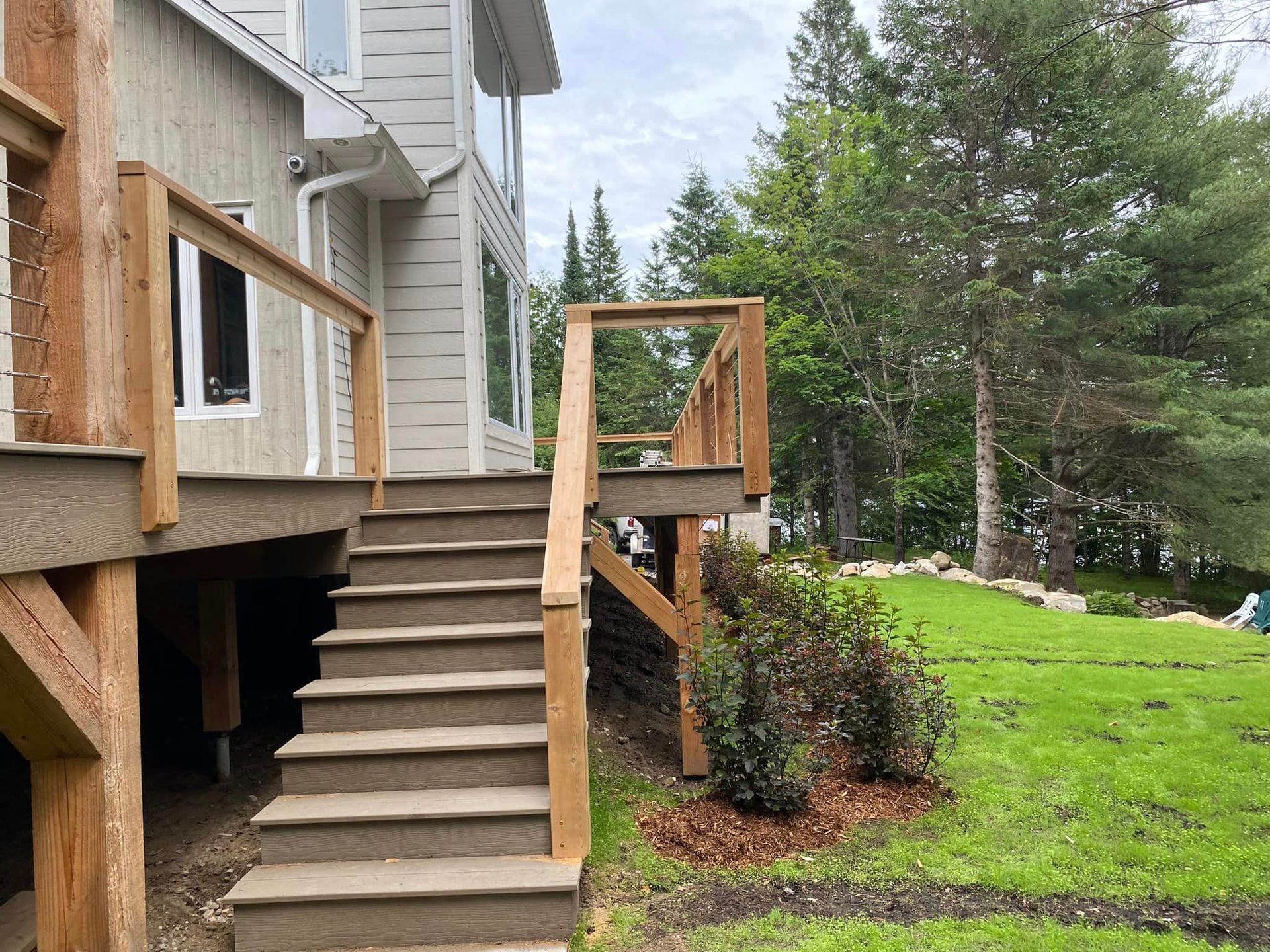 A wooden deck with stairs leading up to it is in the backyard of a house.