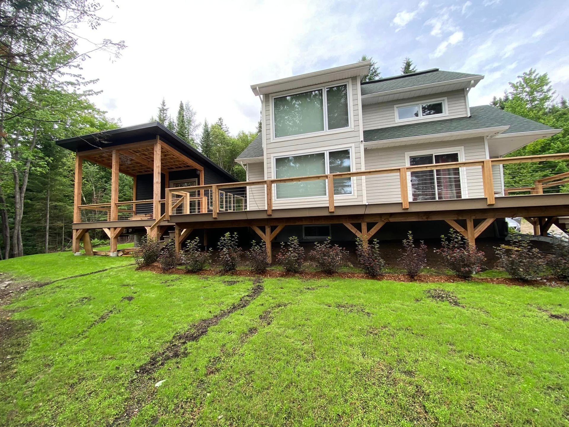 A large house with a large deck in the middle of a lush green field.