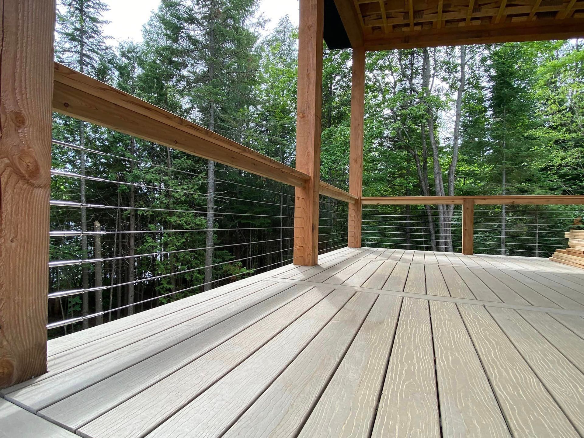 A wooden deck with a metal railing and trees in the background.