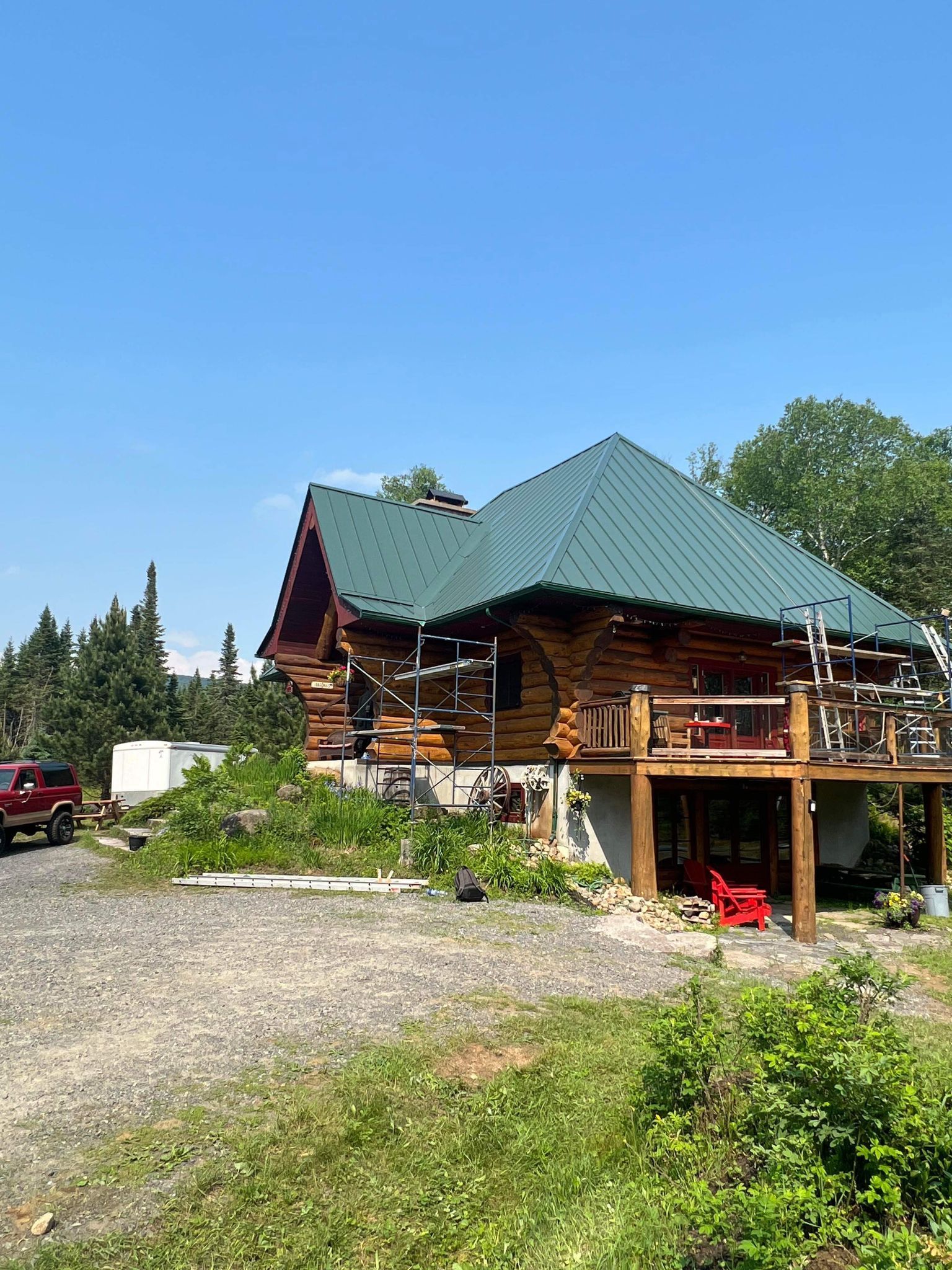 A log cabin with a green roof and a red truck parked in front of it.