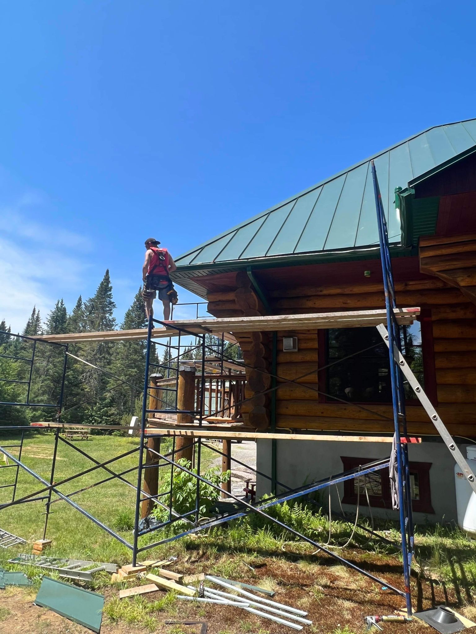 A man is standing on a scaffolding next to a log cabin.