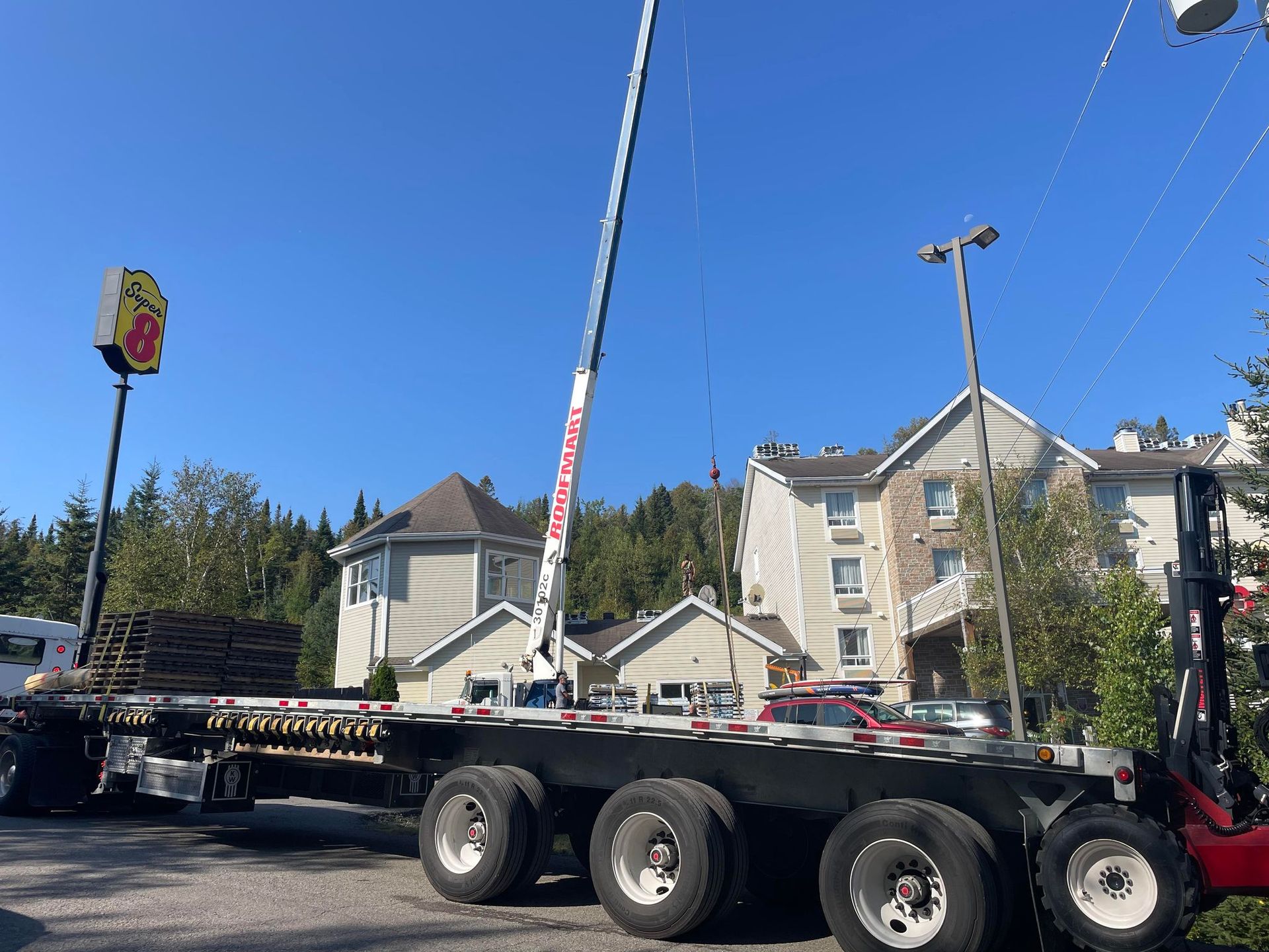 A semi truck with a crane on the back is parked in front of a super 8 restaurant.