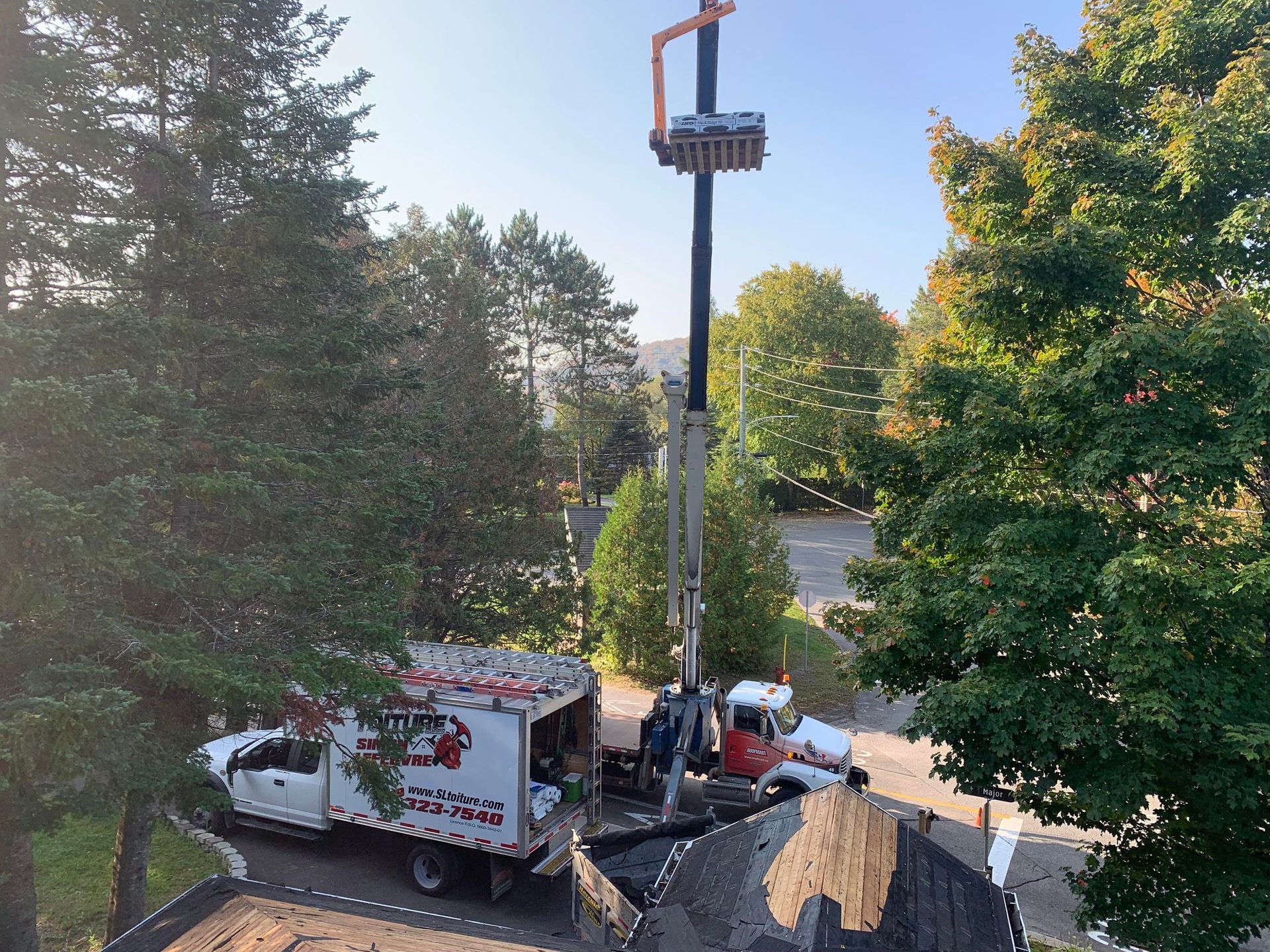 A white truck with a crane on top of it is parked on the side of the road.