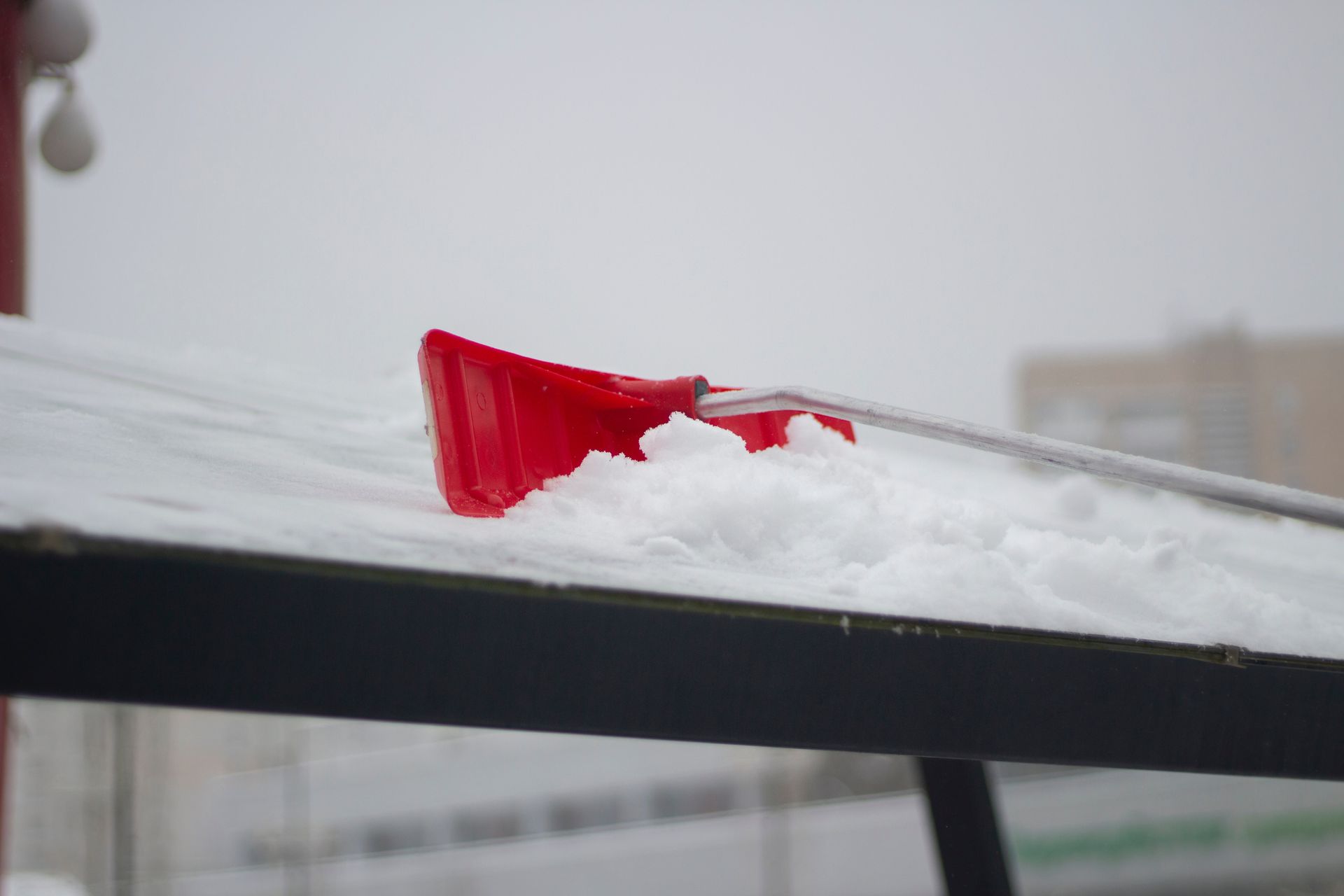 Une pelle à neige rouge est posée sur un toit recouvert de neige.