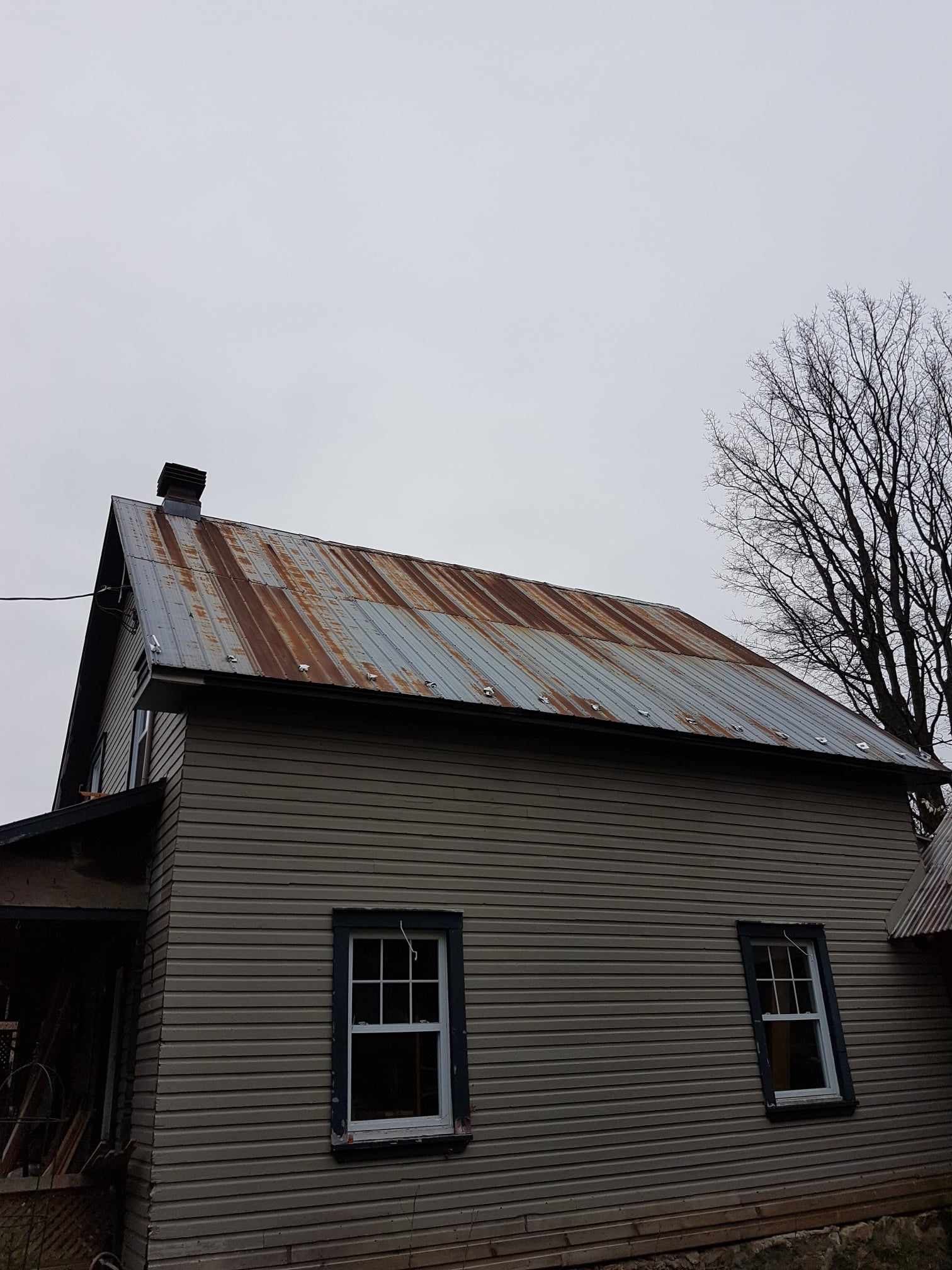 A small house with a rusty metal roof and two windows.