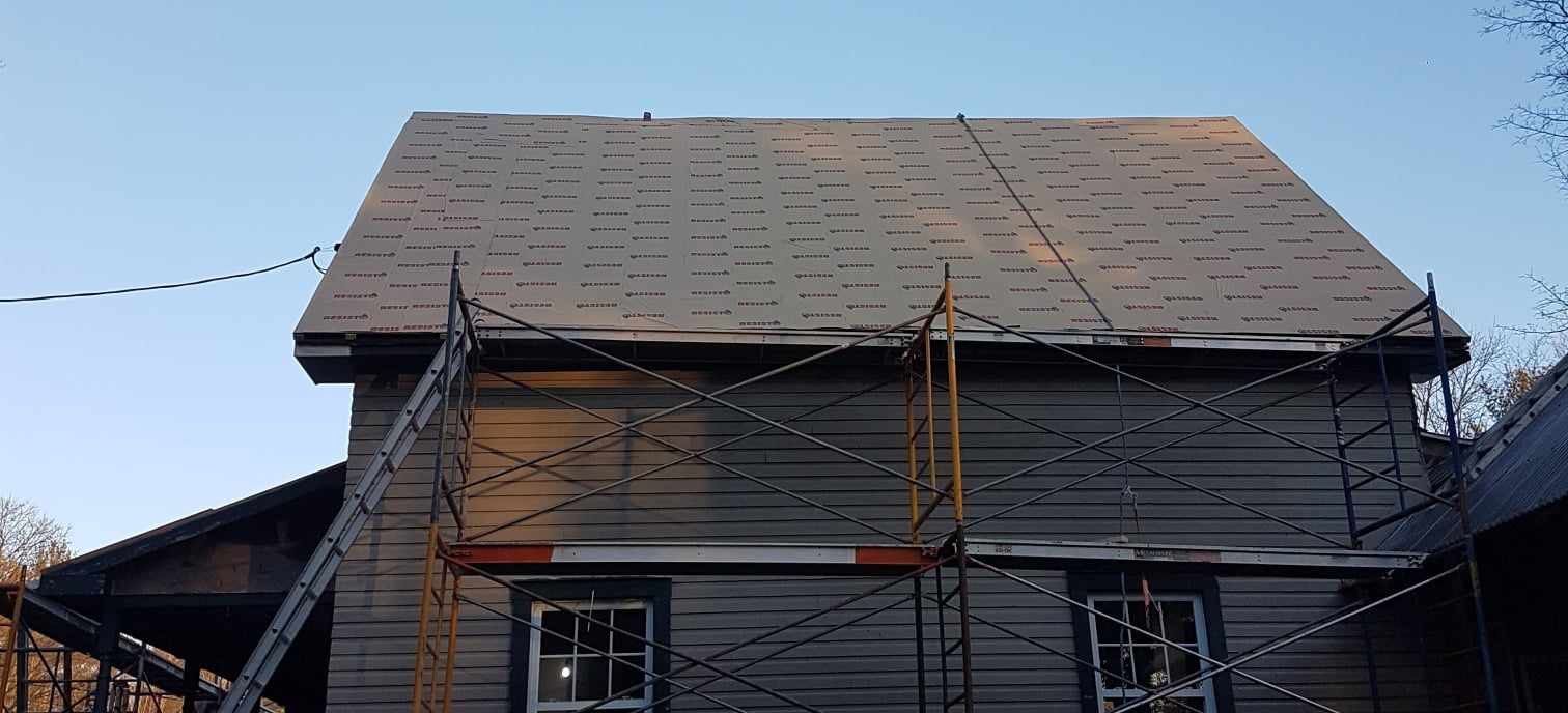 Maison en construction ; échafaudages soutenant les travaux de toiture, ciel bleu clair.