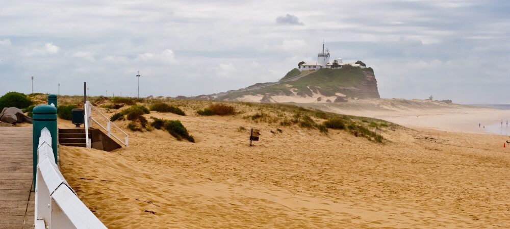 A beach with a lighthouse on top of a hill in the background — Air Conditioning Newcastle