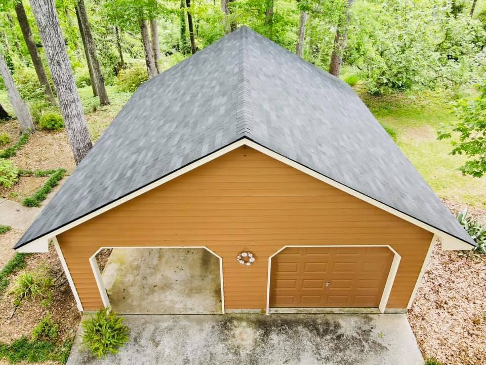 Brown two-car garage with gray shingle roof, surrounded by trees. One garage door is open.