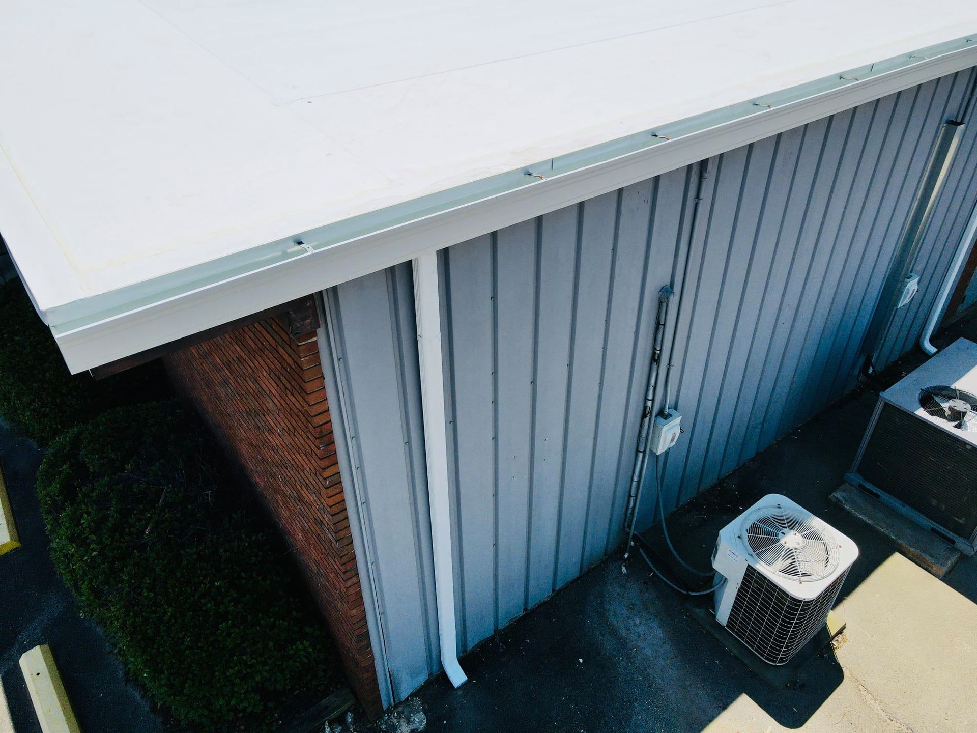 Exterior view of a building with a white roof, grey siding, and air conditioning units.