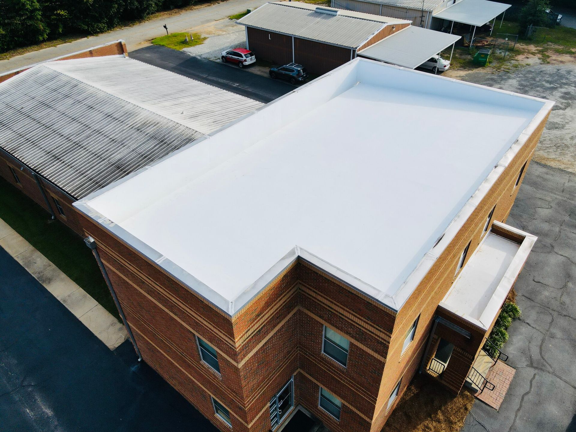 Aerial view of a brick building with a newly installed white flat roof. The roof has a white perimeter.