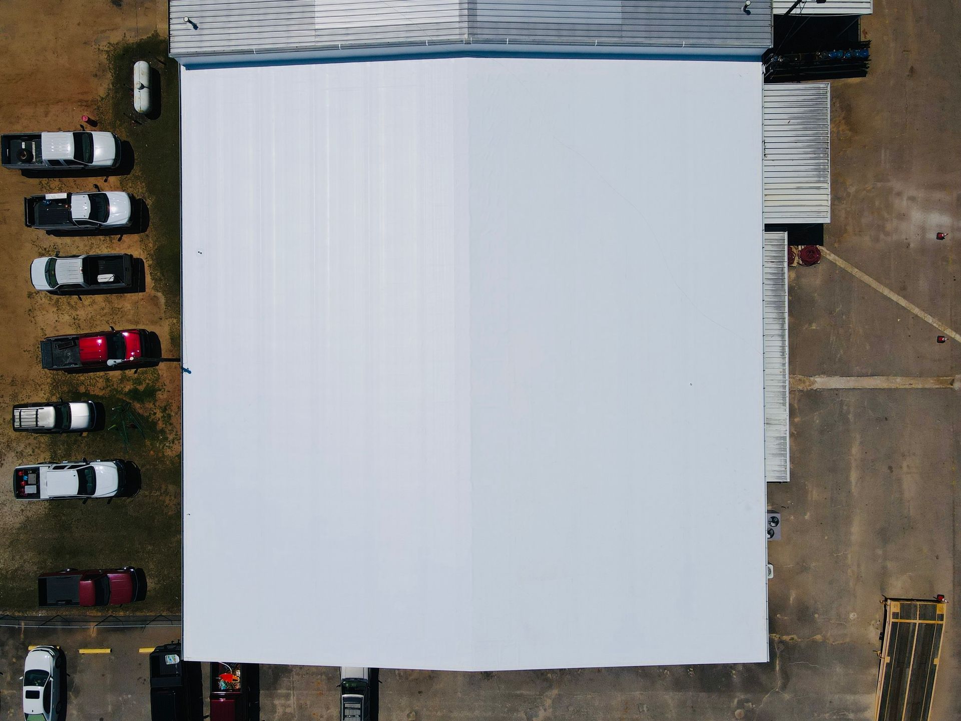 Overhead view of a white-roofed building and parked pickup trucks in a lot.